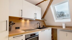 Une cuisine moderne avec des meubles blancs, un plan de travail en bois, un four encastré et une fenêtre au-dessus de l’évier.