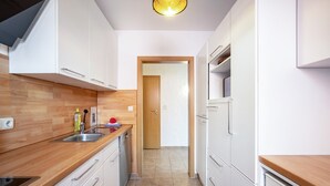 Een moderne keuken met witte kasten, een houten aanrecht en een betegelde vloer.
