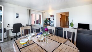 Een moderne woonkamer met een eethoek, een boekenkast en een televisie.