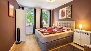 Een slaapkamer met een bed, nachtkastje, lamp en een raam met gordijnen.