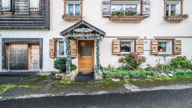 Un edificio con puerta de madera, varias ventanas con contraventanas y un pequeño porche.