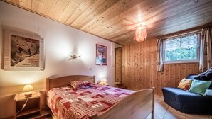 Una habitación con paneles de madera, una cama, una mesita de noche, una lámpara y un ventanal con cortinas.