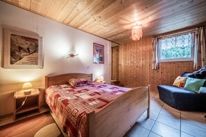 A wooden-paneled room with a bed, bedside table, lamp, and a window with curtains.