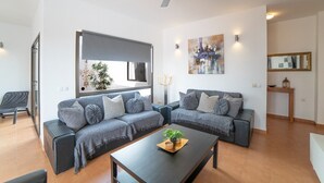 Ein Wohnzimmer mit einem Ecksofa, einem Couchtisch mit Pflanze, einem Deckenventilator und einem großen Fenster.