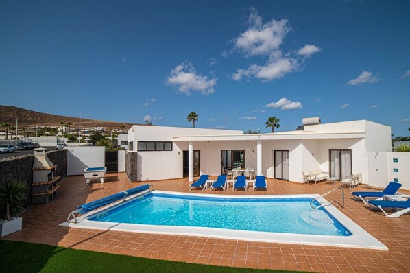 A modern poolside area with a rectangular pool, lounge chairs, and a patio.