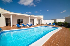 A swimming pool with blue tiles, white pool deck, and blue lounge chairs.