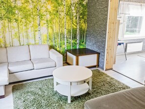 A modern living room with a sofa, a round coffee table, and a decorative wall with a forest mural.