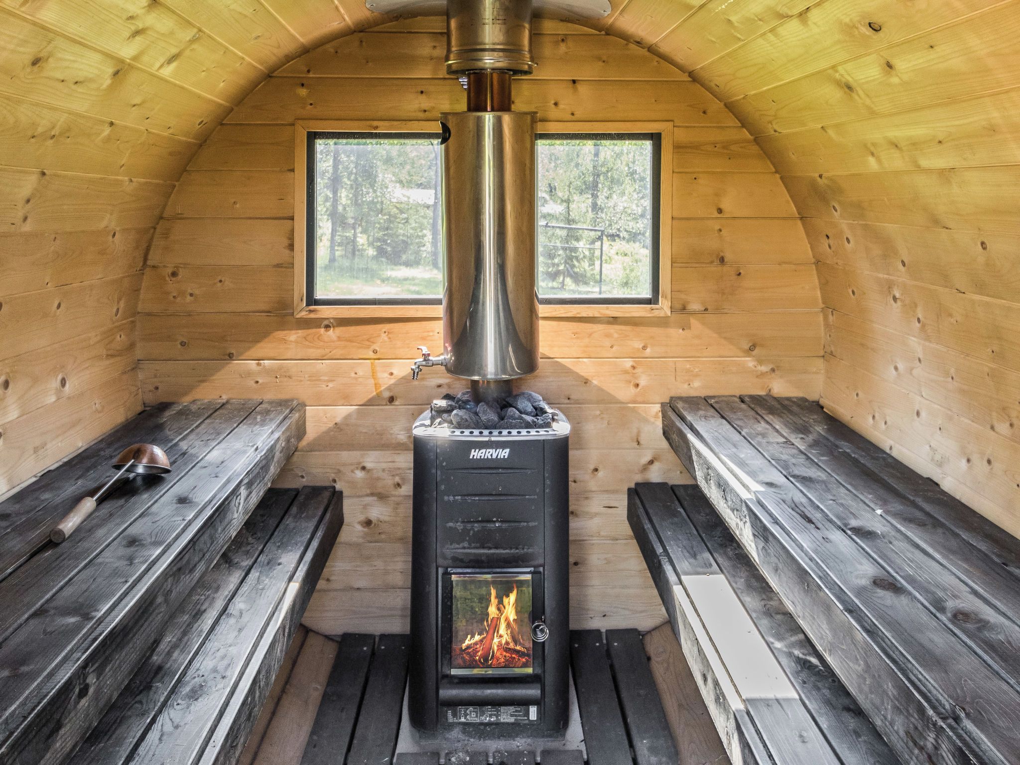 Una cabaña acogedora con estufa de leña, bancos de madera y una ventana que da a un bosque.