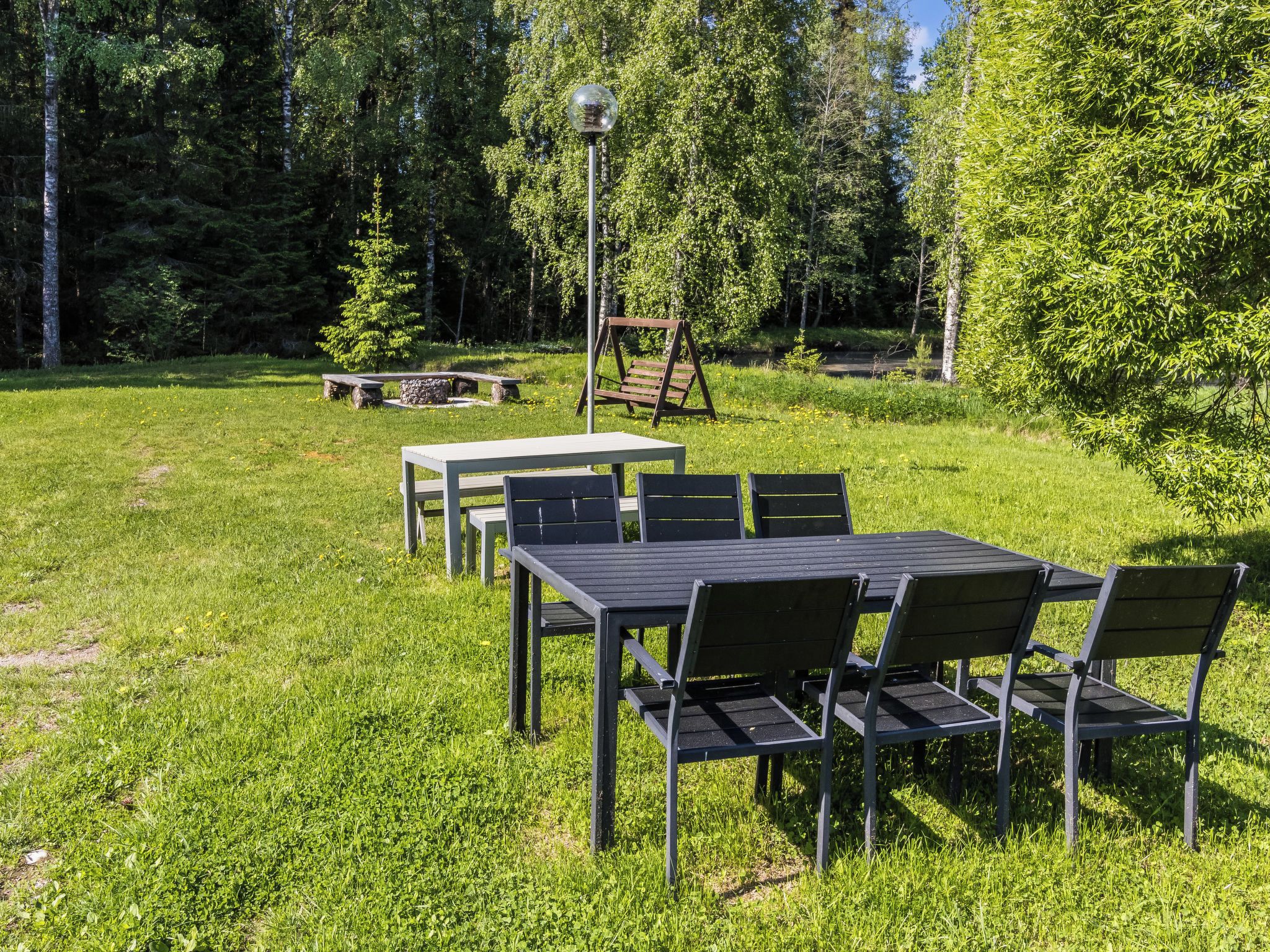 An outdoor seating area with a table and chairs, surrounded by trees and a swing set.
