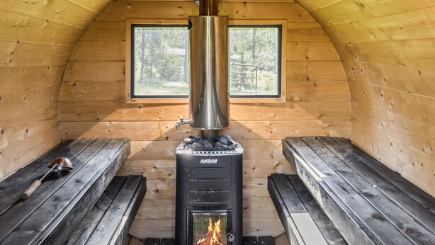 Una cabaña acogedora con estufa de leña, bancos de madera y ventana con vistas a un bosque.