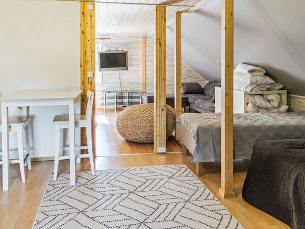 A modern interior with a wooden-framed bed, a desk with chairs, a television, and a patterned rug.