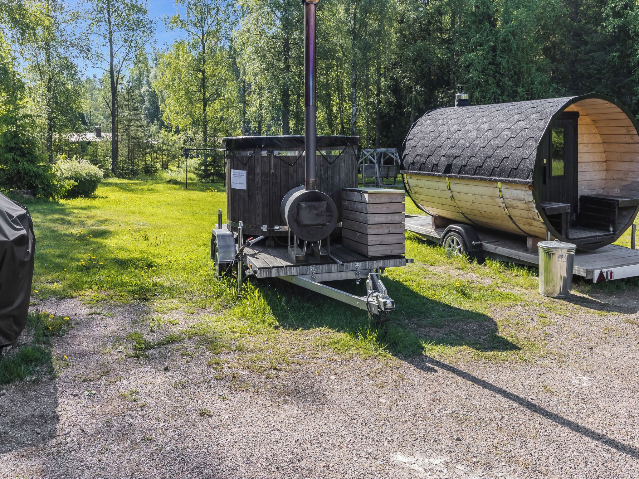 Un poêle à bois portatif et une structure en bois en forme de tonneau, installés dans un espace extérieur verdoyant.