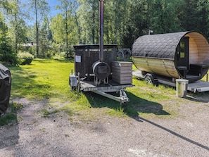 Un poêle à bois portatif et une structure en bois en forme de tonneau, installés dans un espace extérieur verdoyant.