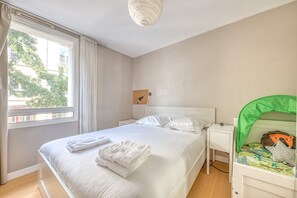 Makuuhuoneessa on sänky, yöpöytä, vihreäkatoksinen sänky, ikkuna, jossa on verhot, ja ikkunasta avautuu näkymä vehreään maisemaan.