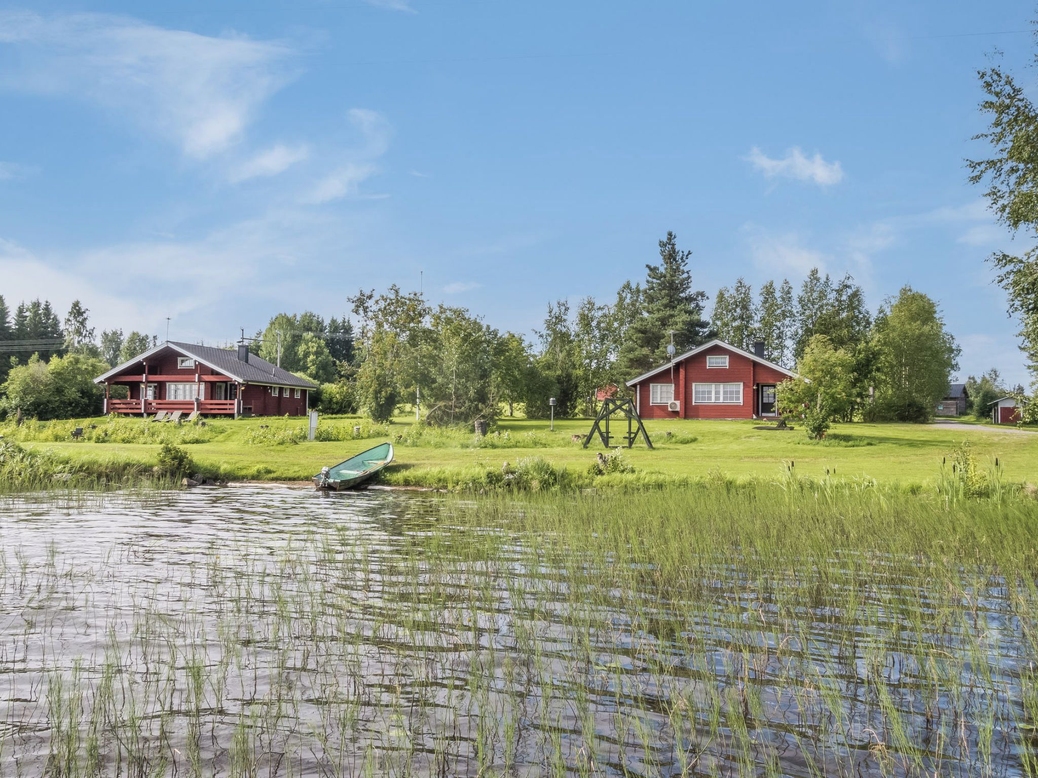 A serene lakeside setting with two red buildings, a boat, and lush greenery.