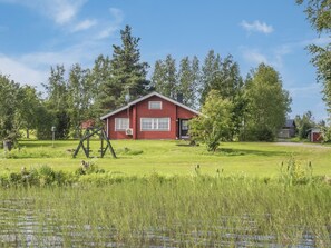Ein rotes Haus mit einer Veranda, umgeben von einem grasbewachsen Feld und Bäumen.
