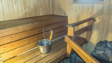 Una sauna con bancos de madera, un cubo metálico y un recipiente de piedra.