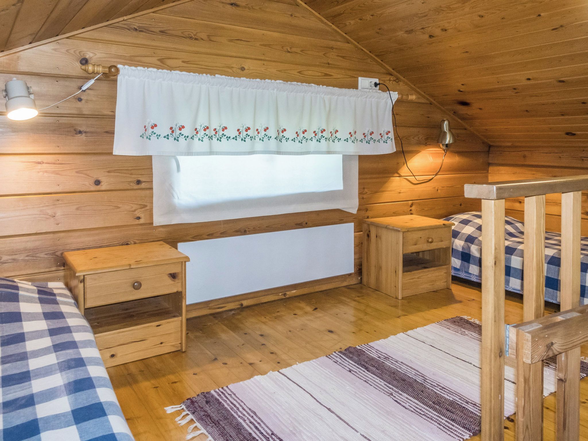 Una habitación tipo cabaña acogedora, con detalles de madera, una ventana con cortina blanca, una mesita de noche y un edredón a cuadros.