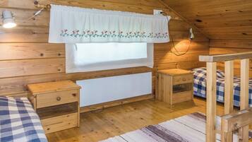 Una habitación tipo cabaña acogedora, con detalles de madera, una ventana con cortina blanca, una mesita de noche y un edredón a cuadros.