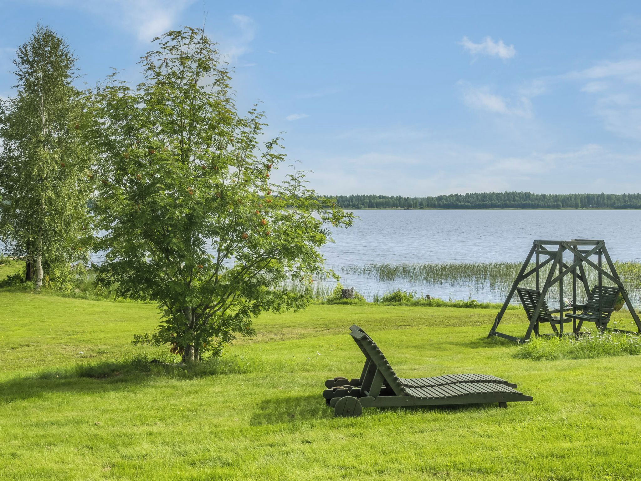 Un área verde con un columpio y una silla de reclinación junto a un lago.