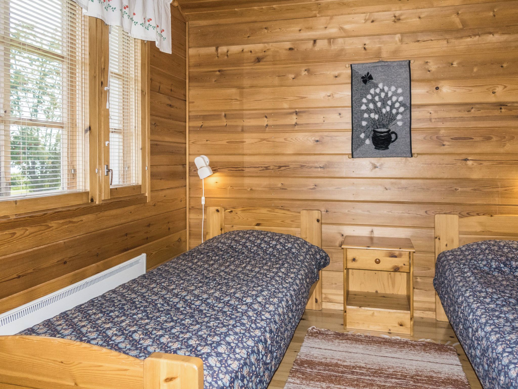Een kamer in chaletstijl met twee houten bedden, een klein tafeltje, een wandlamp en een raam met zonwering.