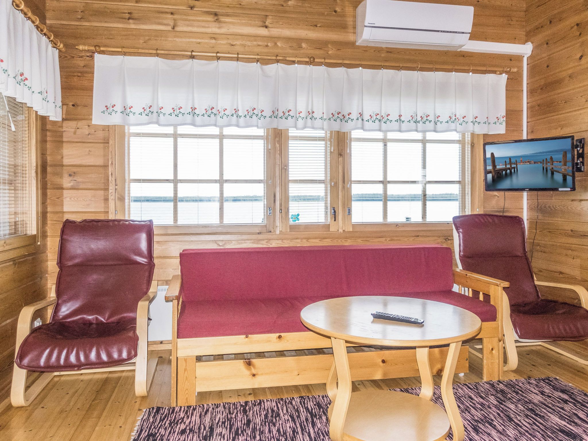 Une cabane en bois avec un canapé, deux fauteuils, une petite table et un téléviseur fixé au mur.
