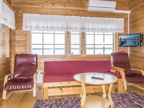 Eine Holzhütte mit einer Couch, zwei Stühlen, einem kleinen Tisch und einem Fernseher an der Wand.