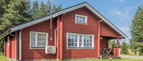 Una casa de madera roja con dos ventanas, un porche y un equipo de aire acondicionado.