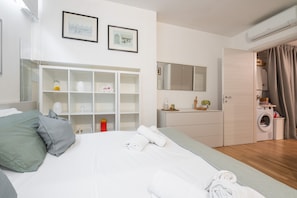 Une chambre d’hôtel moderne équipée d’un lit, d’une armoire, d’un miroir, d’une machine à laver et d’une petite salle de bain.