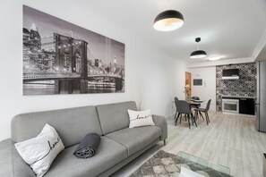 Un salon moderne avec un canapé gris, un tableau représentant un paysage urbain et un coin repas comprenant une table et des chaises.