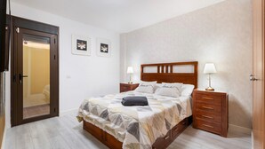 Un dormitorio con una cama de madera, dos mesitas de noche, un armario y una puerta que da a otra habitación.