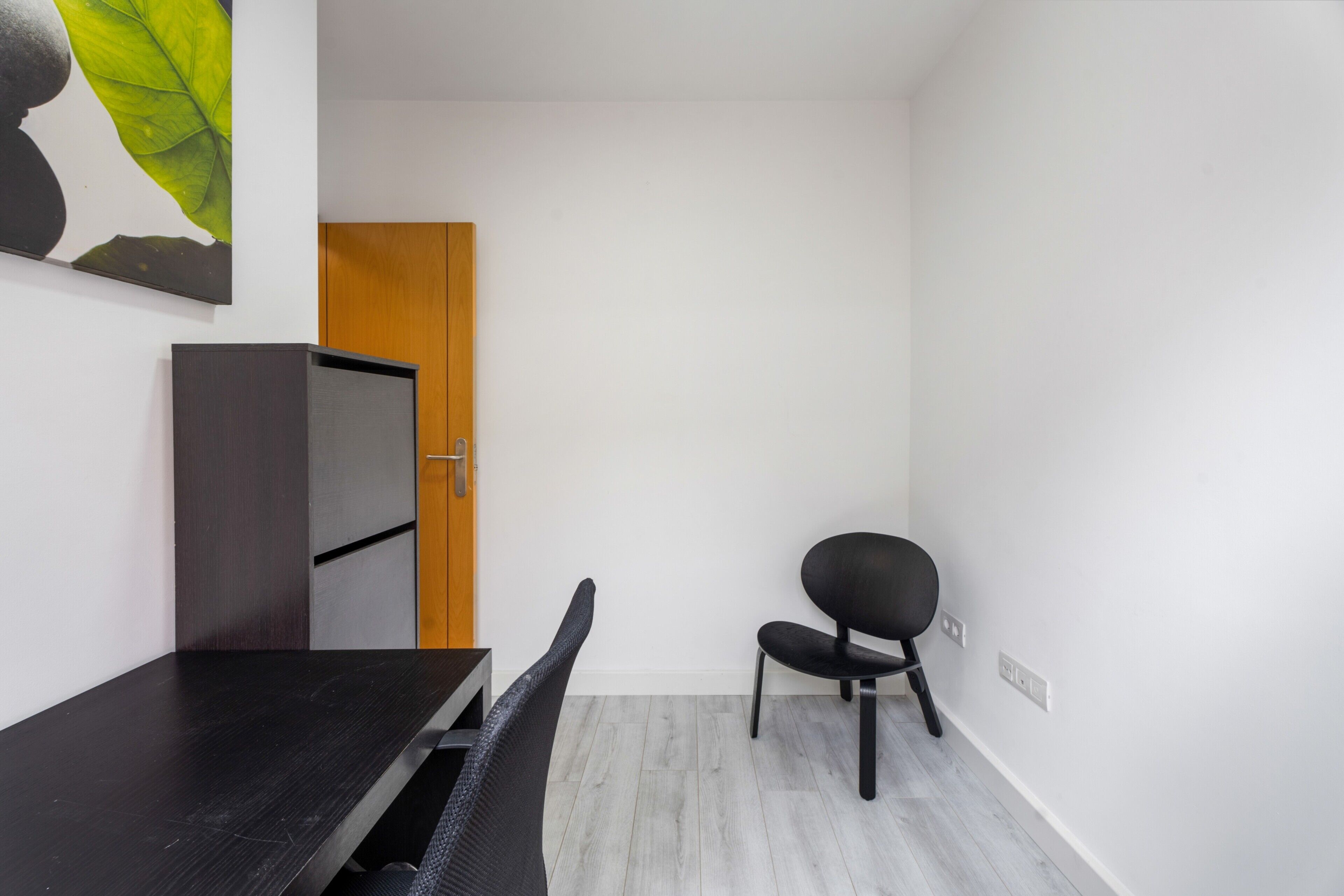 A room with a dark wooden desk, a black chair, a wooden door, and a white wall.