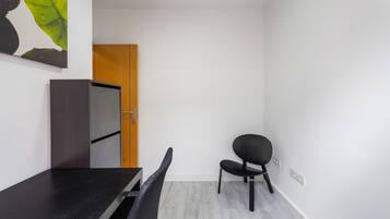 A room with a dark wooden desk, a black chair, a wooden door, and a white wall.