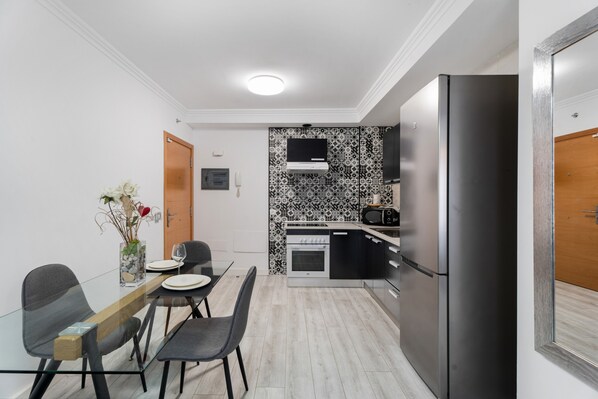 Una cocina moderna con comedor, que incluye una mesa de vidrio, sillas, un refrigerador y un microondas.