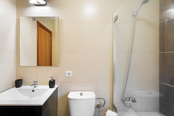 A bathroom with a sink, mirror, toilet, and shower.