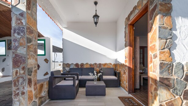 Un patio de paredes de piedra con mobiliario exterior, un felpudo e iluminación colgante.