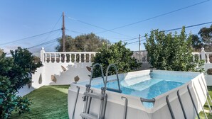 Una piscina con escalera, rodeada por una cerca blanca y vegetación.