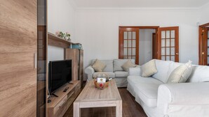 Una sala de estar con televisión, un mueble de madera, un sofá, una mesa de centro y una puerta.