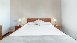 Una cama bien hecha con sábanas blancas, dos lámparas de noche y un cabecero de madera en una habitación de hotel.
