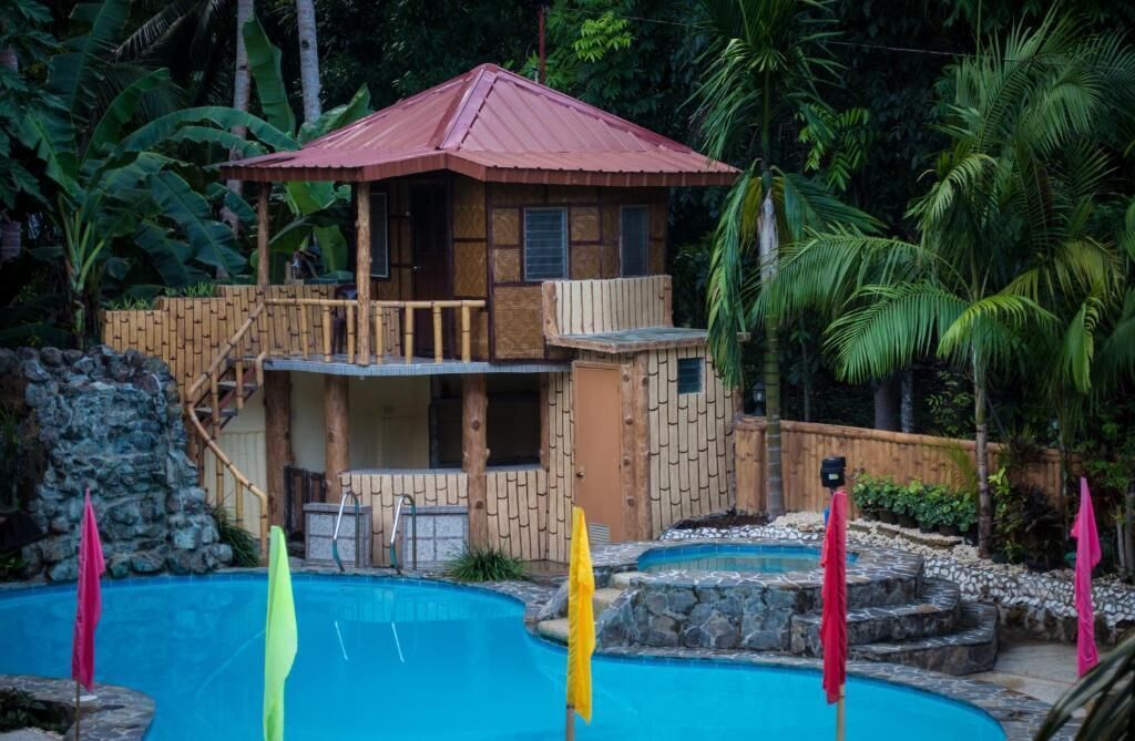 Une maison en bois avec un toit rouge, une piscine et un escalier menant à un balcon.