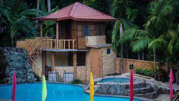 Une maison en bois avec un toit rouge, une piscine et un escalier menant à un balcon.