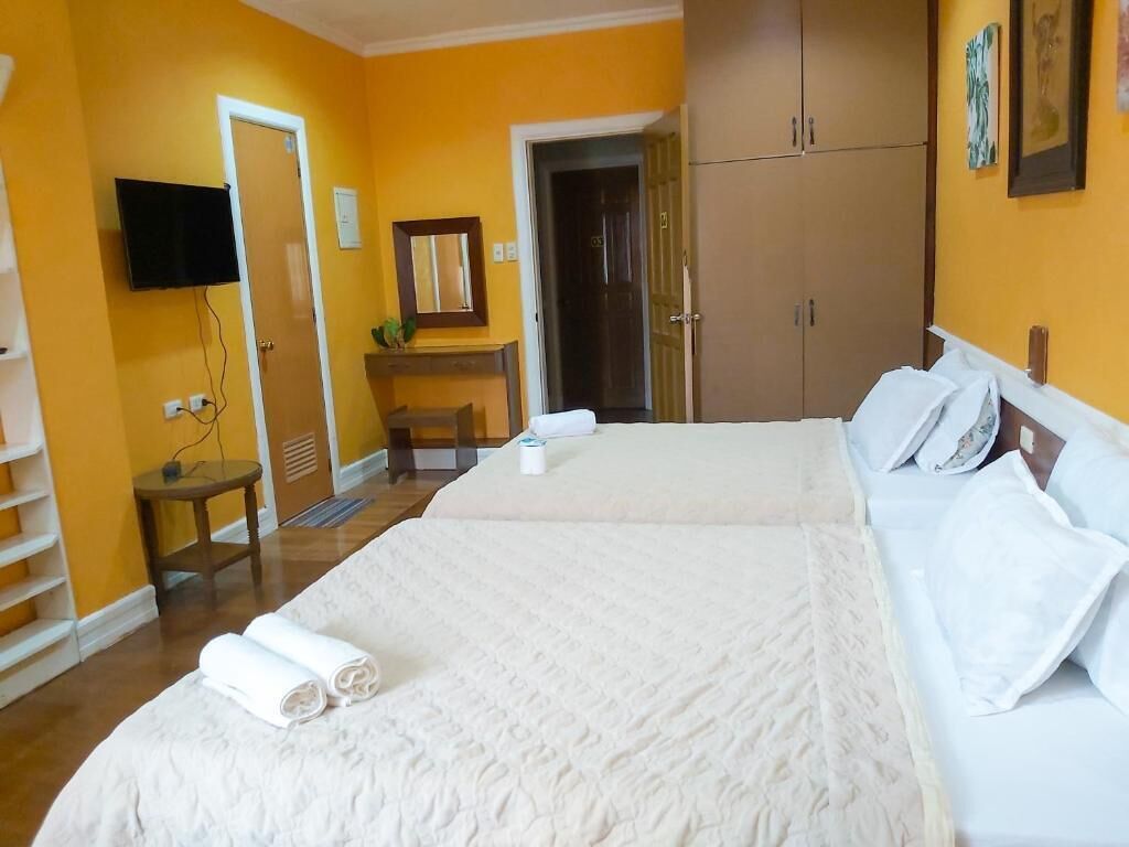 A hotel room with a bed, a television mounted on the wall, a wardrobe, and a door leading to another room.