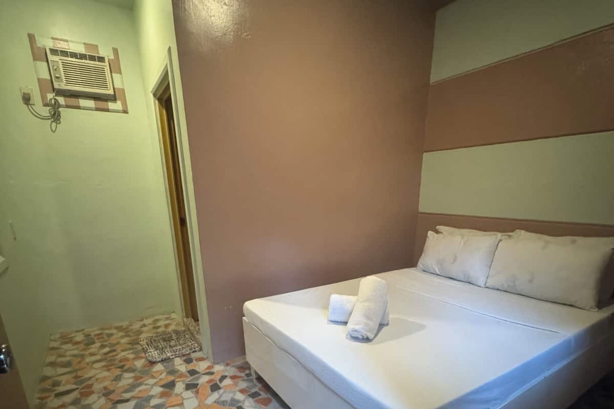 A hotel room with a bed, a patterned floor, a wall-mounted air conditioning unit, and a door.