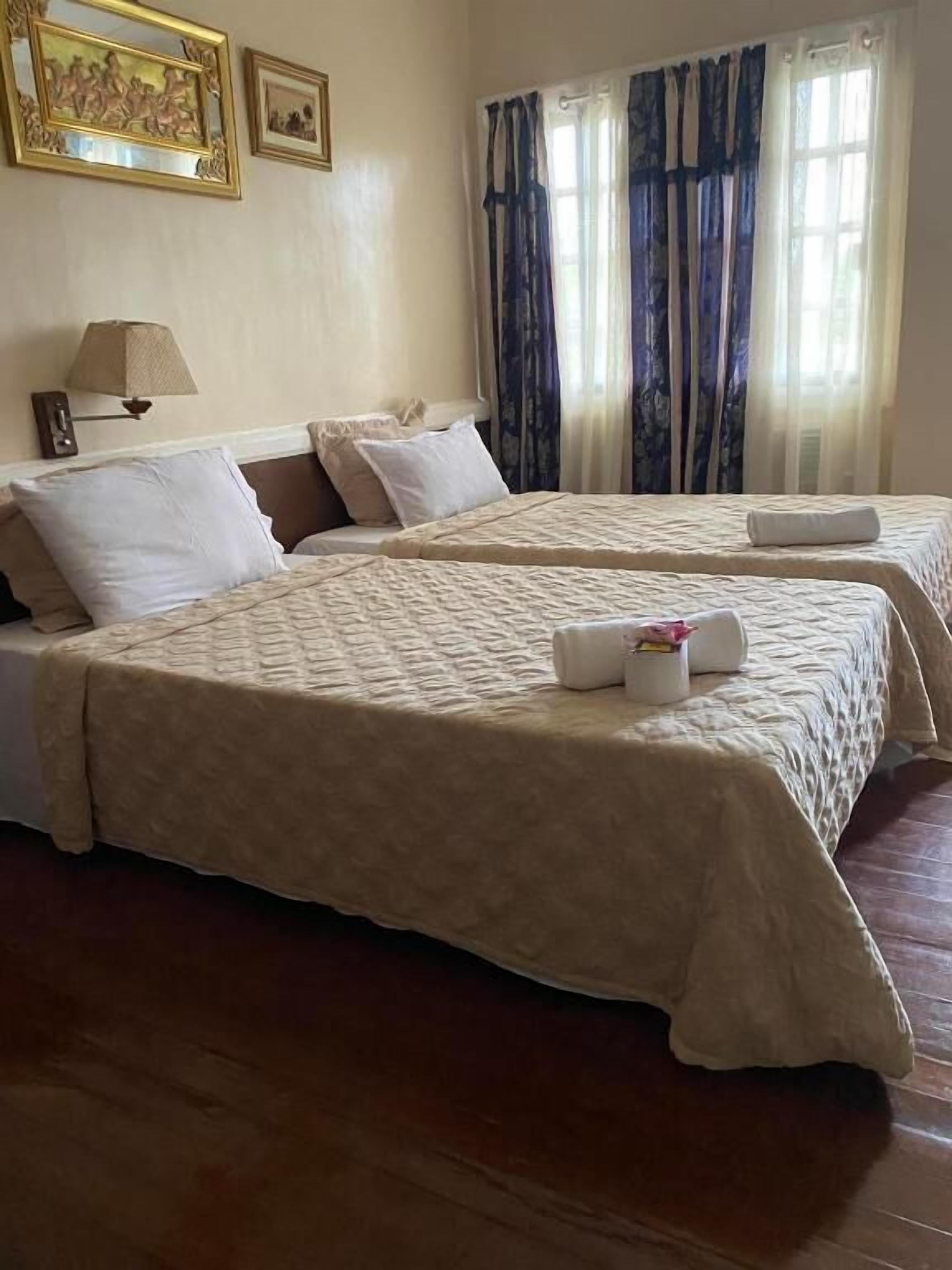 A hotel room with two beds, a lamp, and curtains.