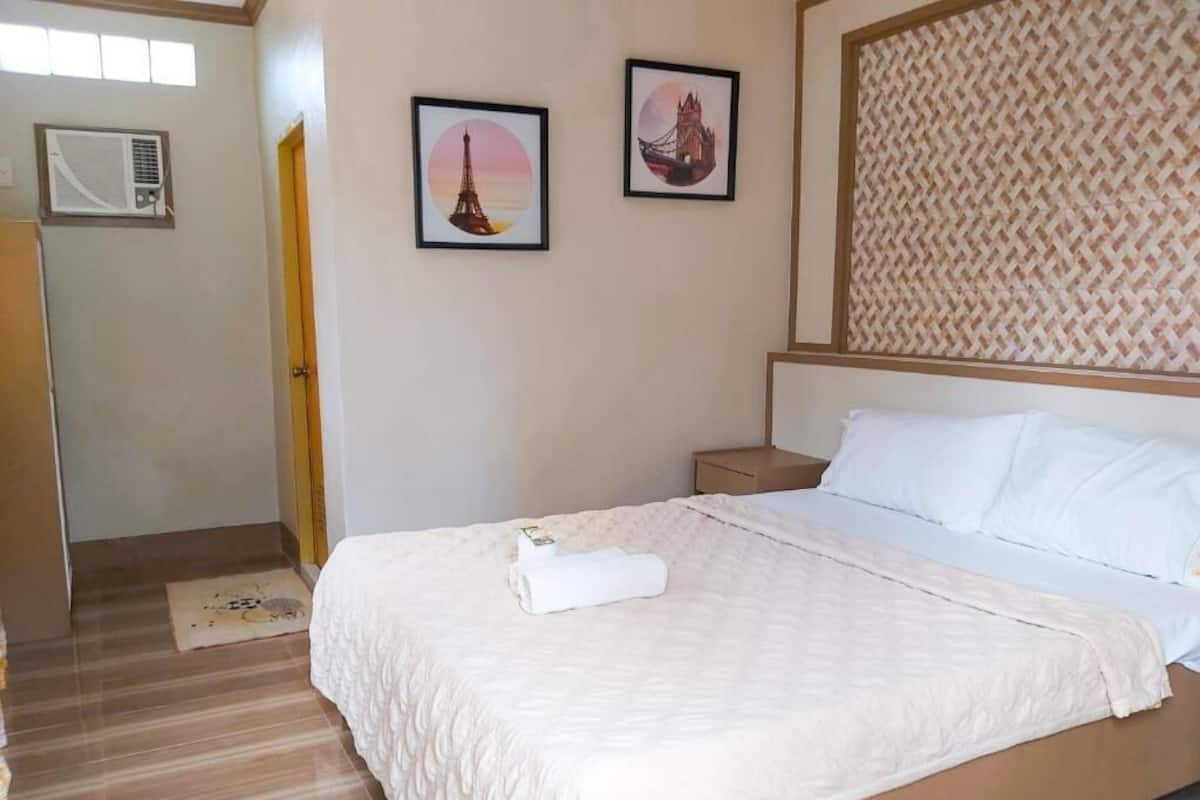 A bedroom with a bed, a nightstand, a wall-mounted air conditioner, and two framed pictures.