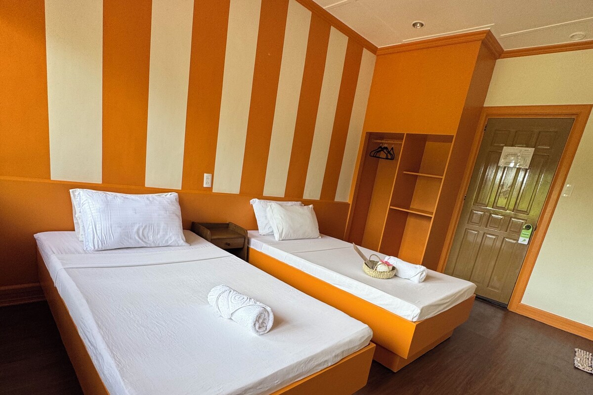 A hotel room with two beds, wooden flooring, and a striped wall design.