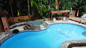 Une piscine bordée de pierres, une terrasse en bois et un belvédère.