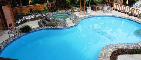 A swimming pool with a stone border, a wooden deck, and a gazebo.