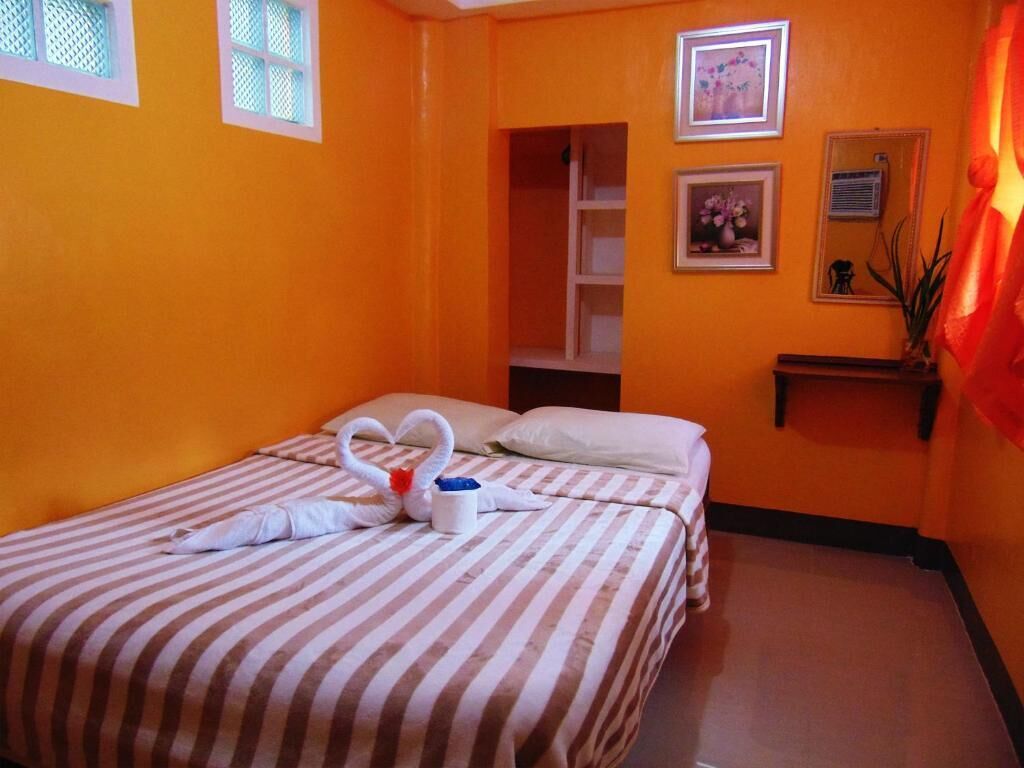 Habitación de hotel con paredes anaranjadas, una cama con ropa de cama a rayas, una toalla con forma de cisne y dos cuadros en la pared.