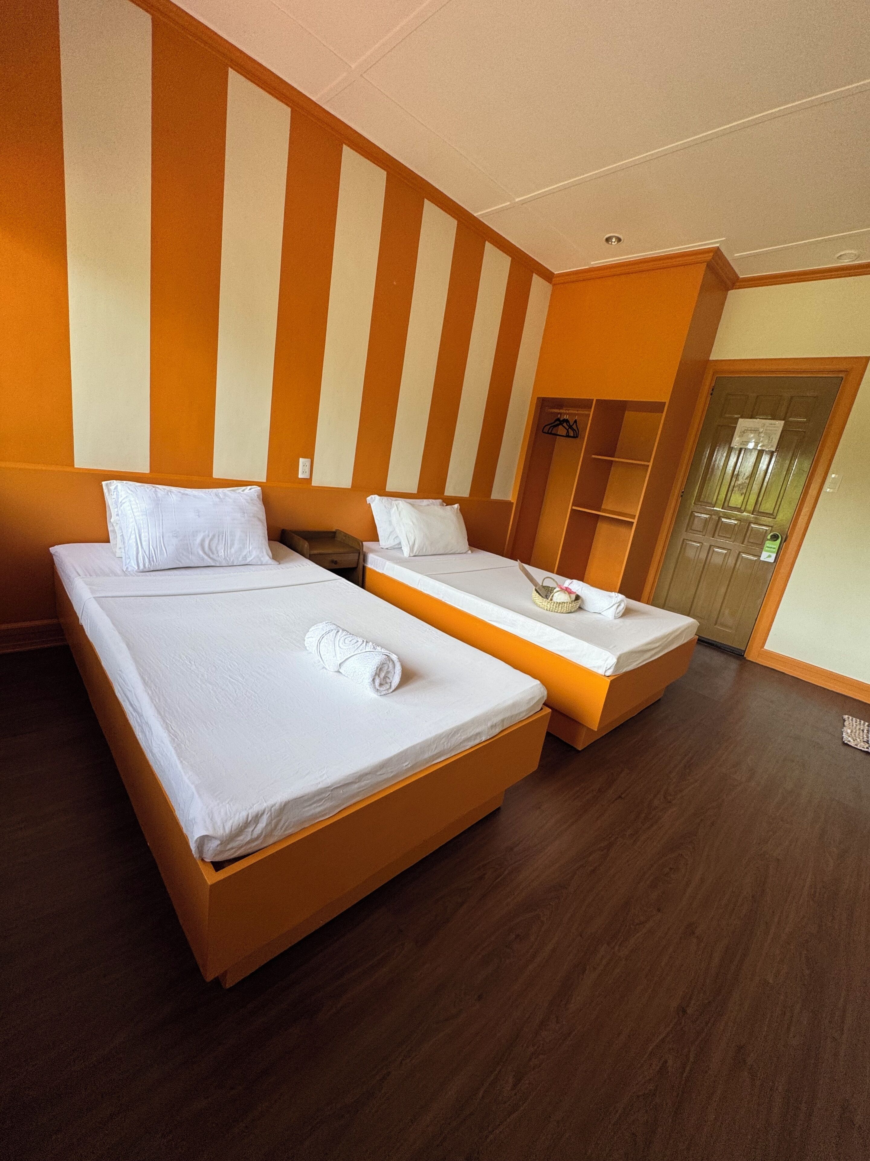 Ein Hotelzimmer mit zwei Betten, Holzboden und einem Streifenmuster an der Wand.